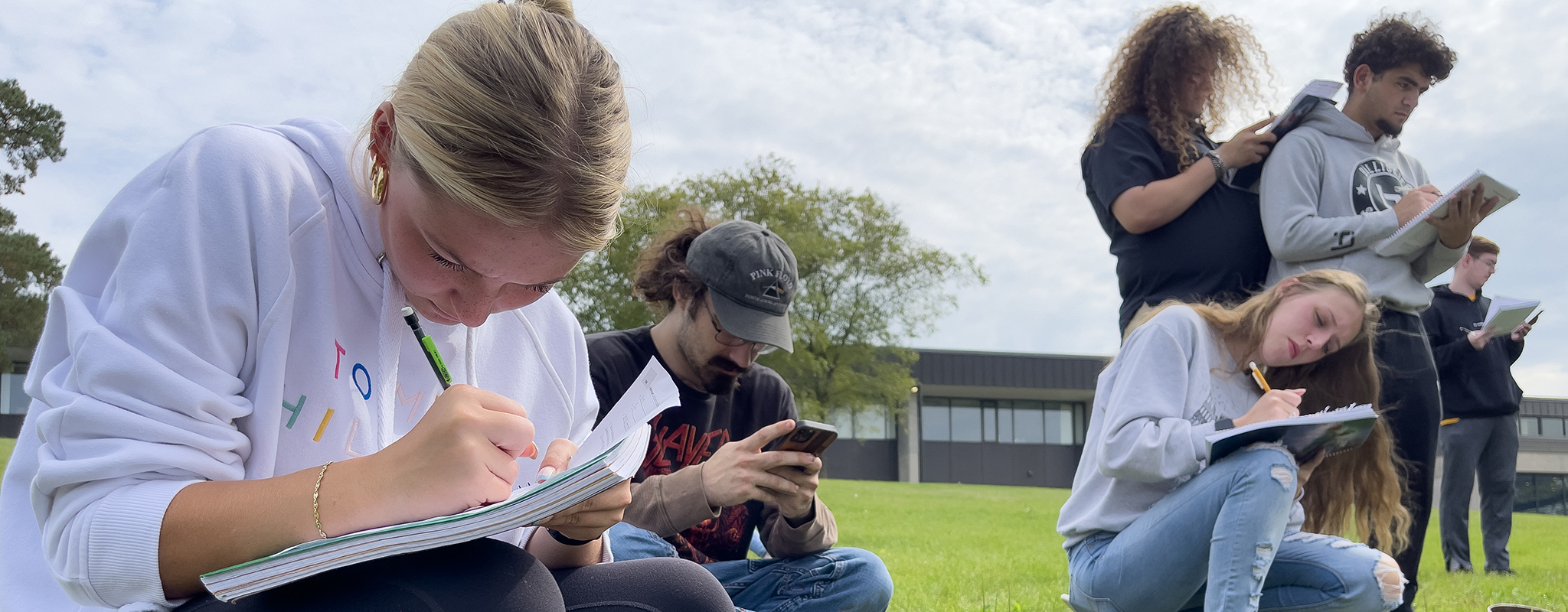 student outside writing on notebooks.