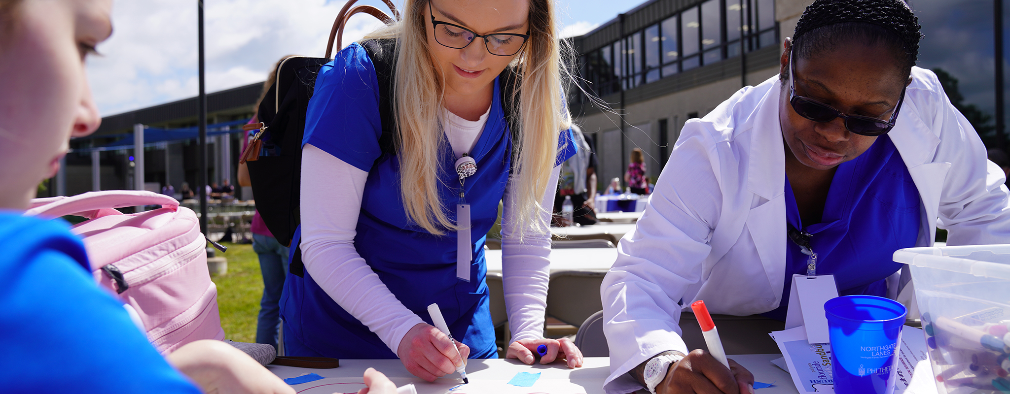 three women in scrubs writing on posters.