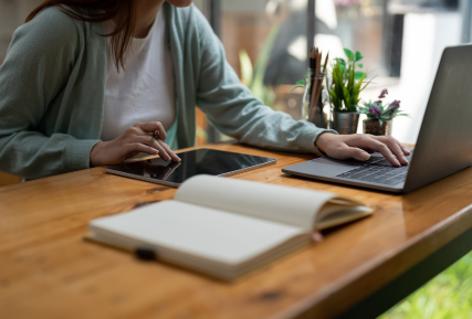 person at a desk with a laptop, tablet and book