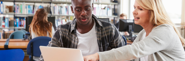 student and teacher sitting at a table looking at a laptop