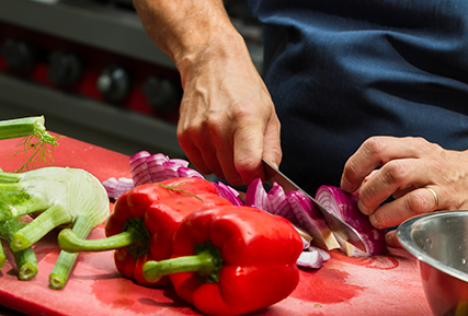 person cutting a red onion in a commercial kitchen.