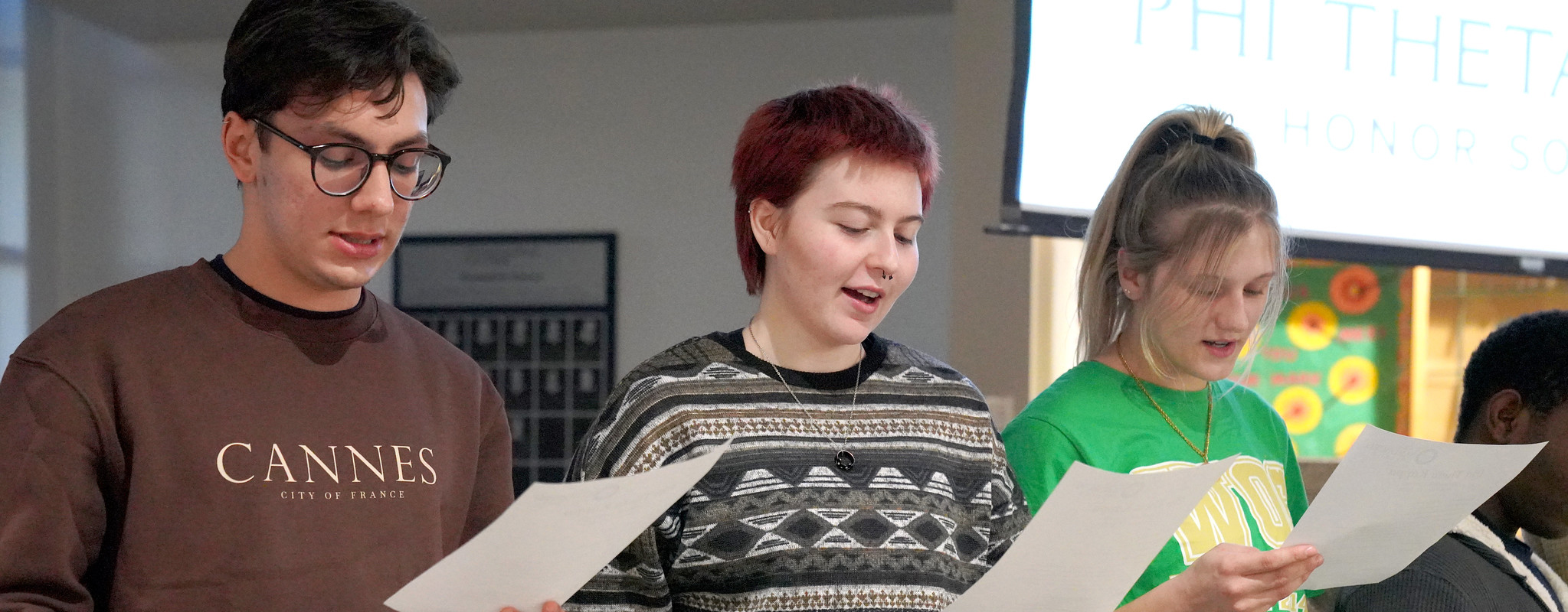 three students looking reading off a paper in front of a crowd.