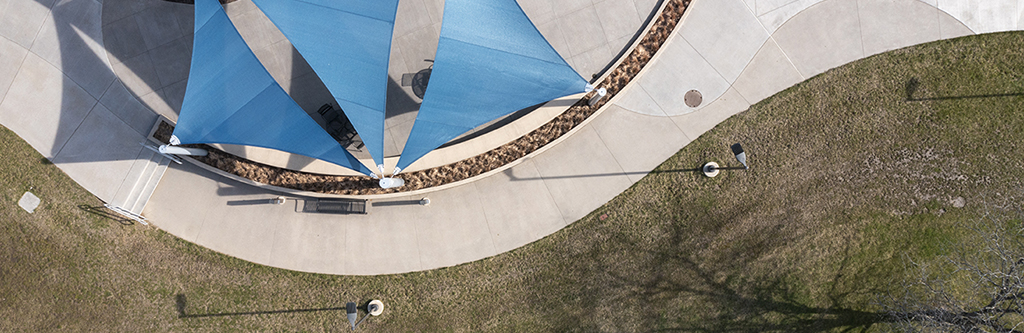 Drone photo of the patio, showing grass and sidewalk with triangular sun shades over the top.