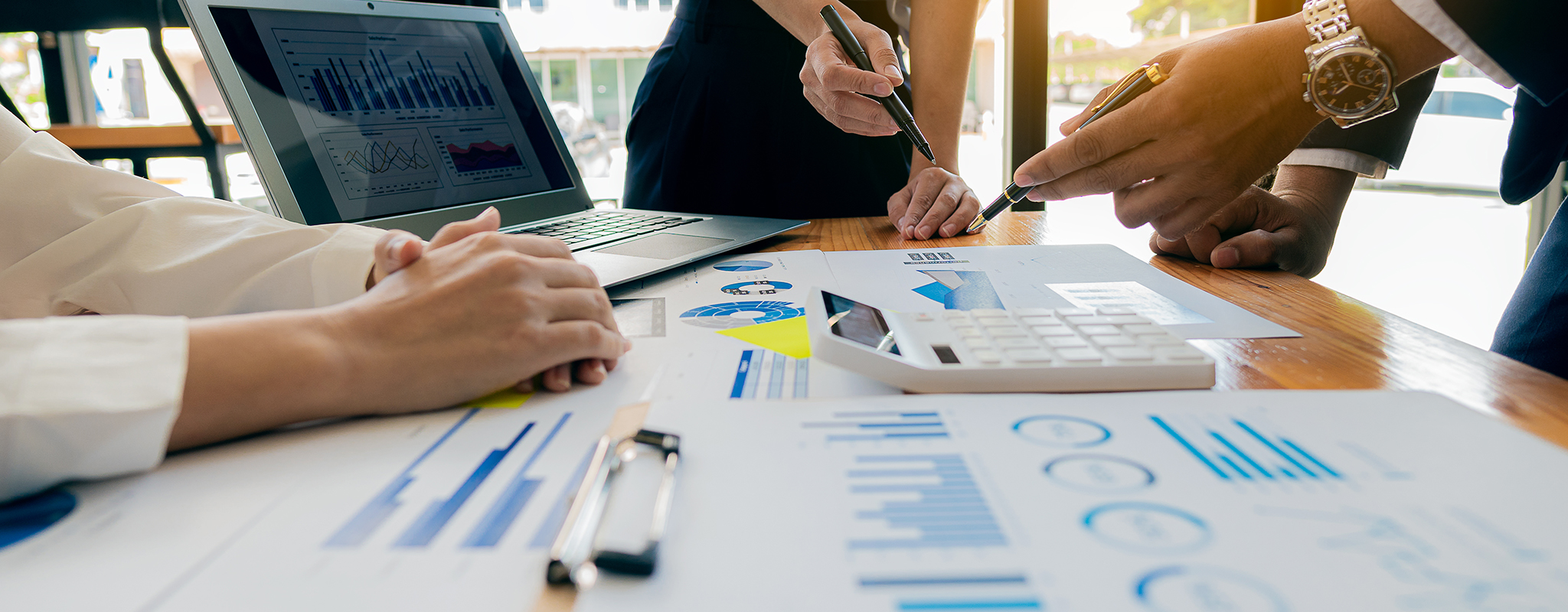 office setting with a table on spreadsheets and three people standing pointing at them.