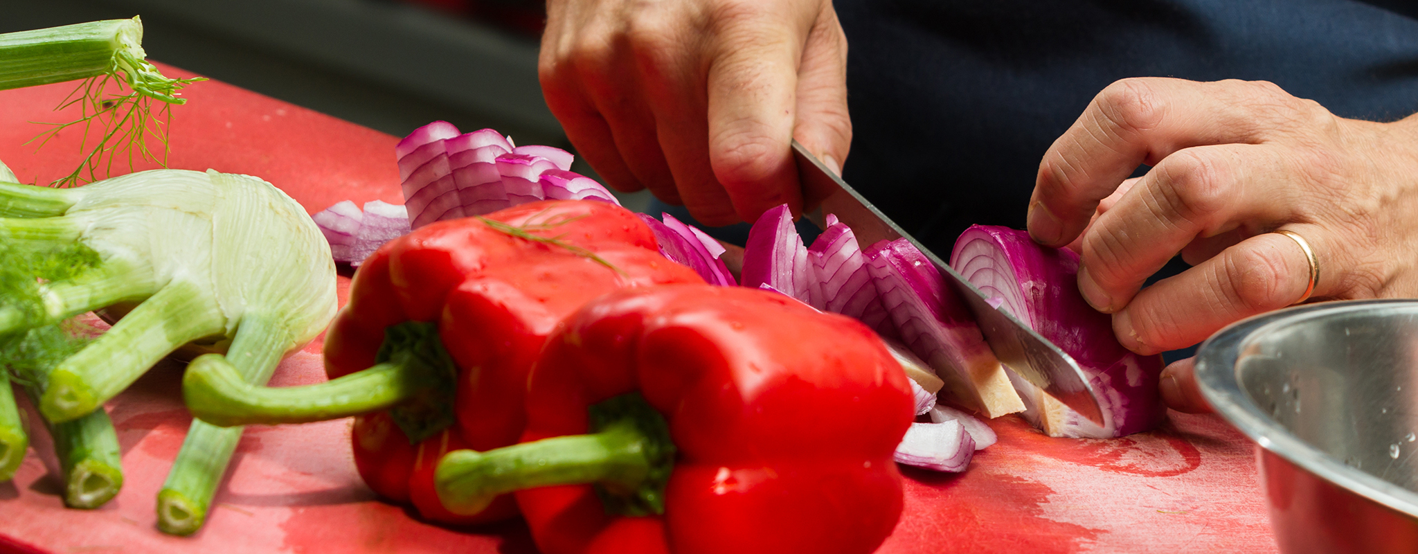 person cutting a red onion on a cutting board in a kitchen.