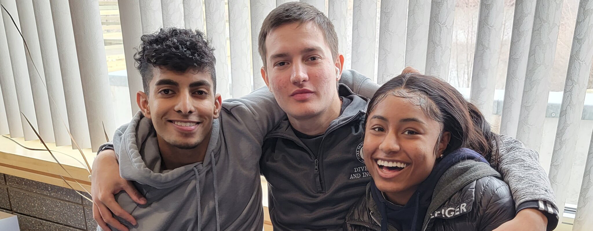 three students smiling sitting on a bench in the hallway.