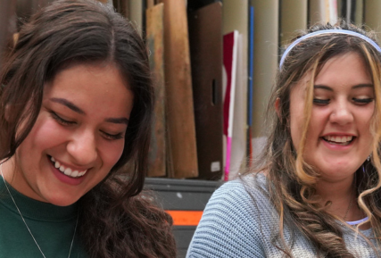 two women smiling while working on art projects.