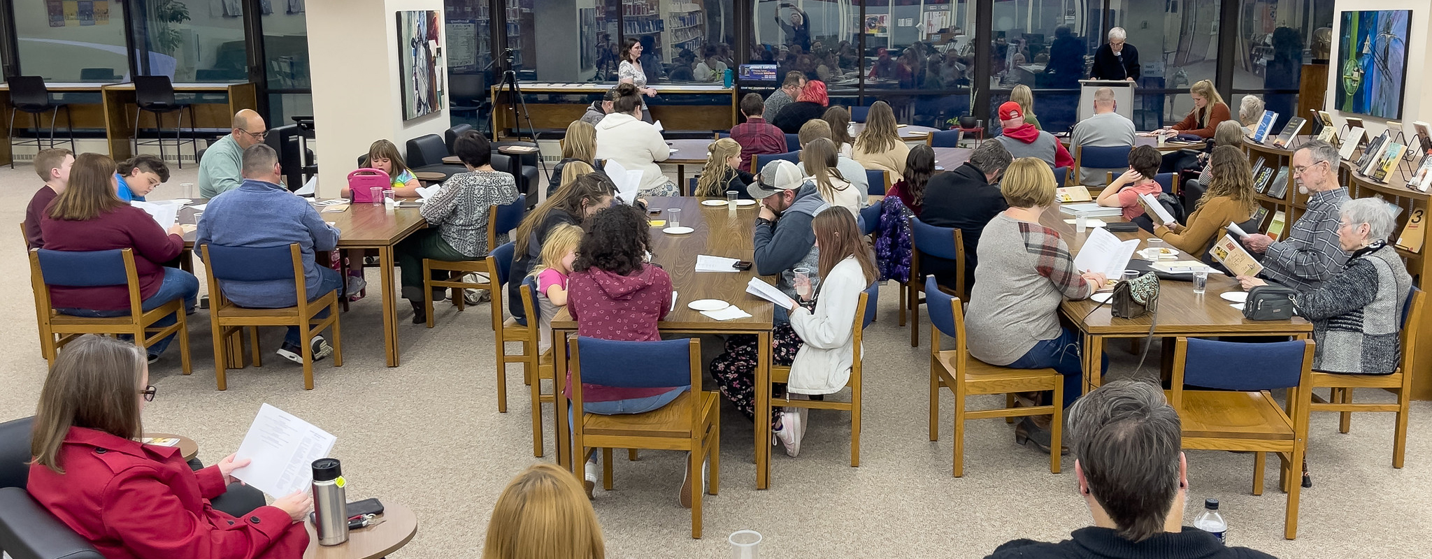 larger group of people sitting in the library listening to people reading poetry.